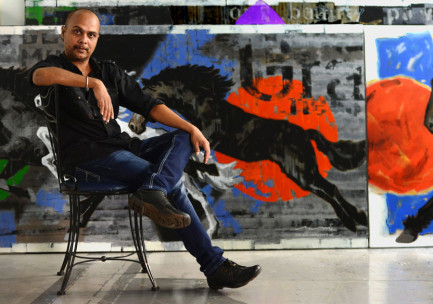 Artist Devidas Dharmadhikari sitting beside a monumental horse painting in progress in his Pune studio